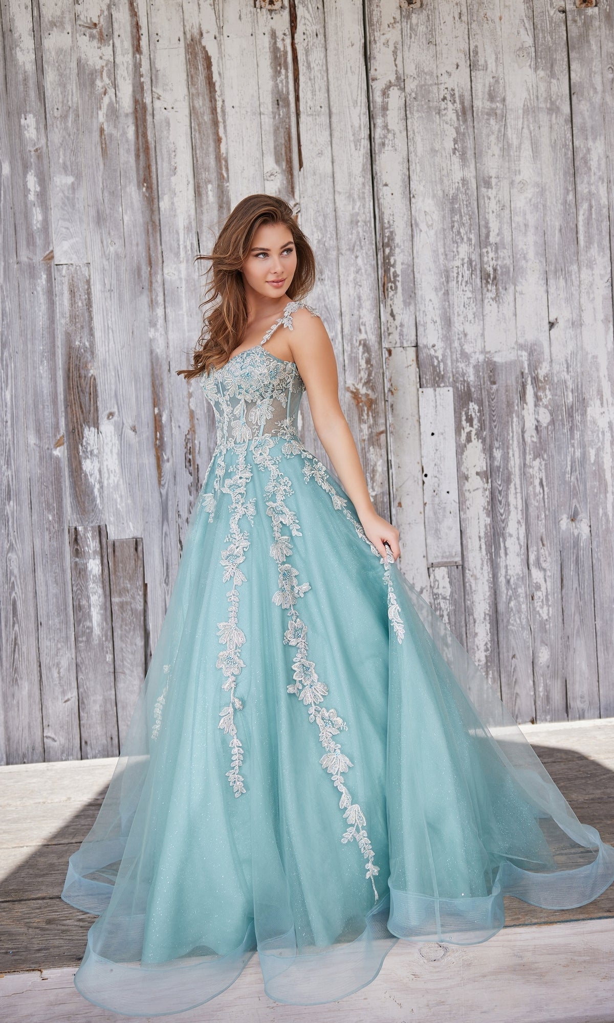 A woman in the Metallic-Lace Colette Long Tulle Prom Dress CL5165 stands in front of a weathered wooden wall.